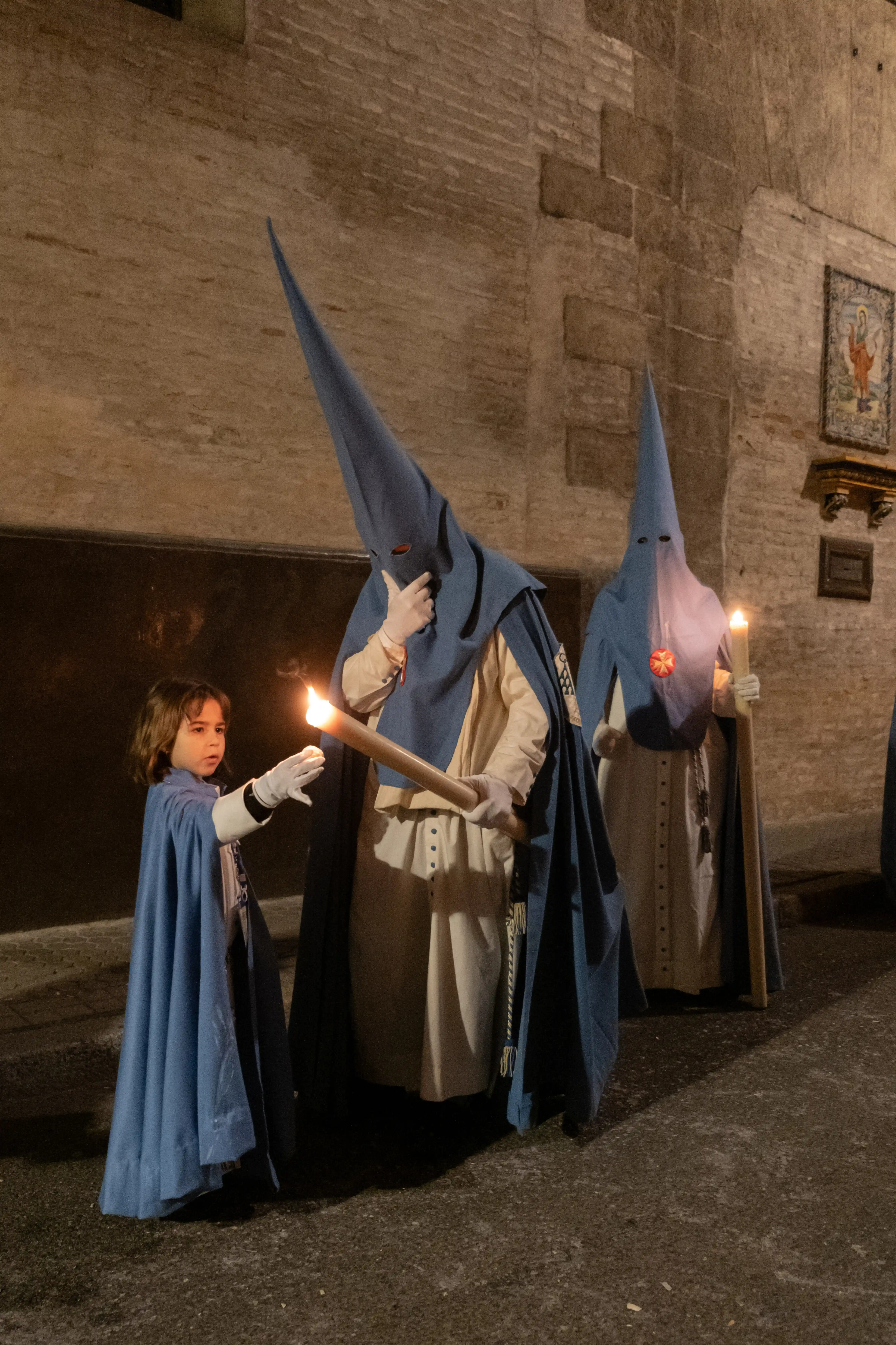 Segundo premio 2024 fotografía Semana Santa Hispano Happiness Club – nazareno ayudando a un niño a encender un cirio.